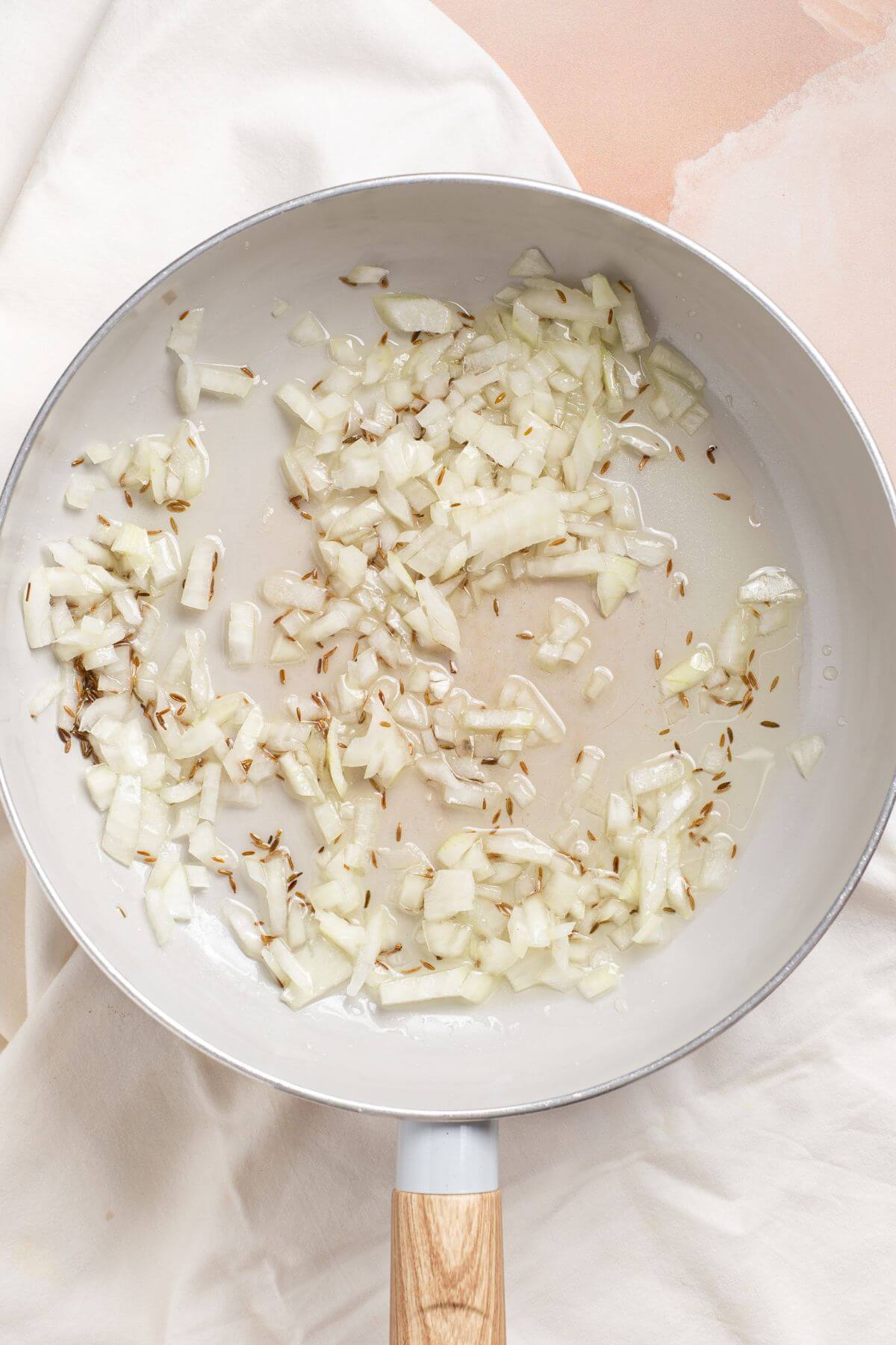 Sautéing onions in skillet with cumin seeds.