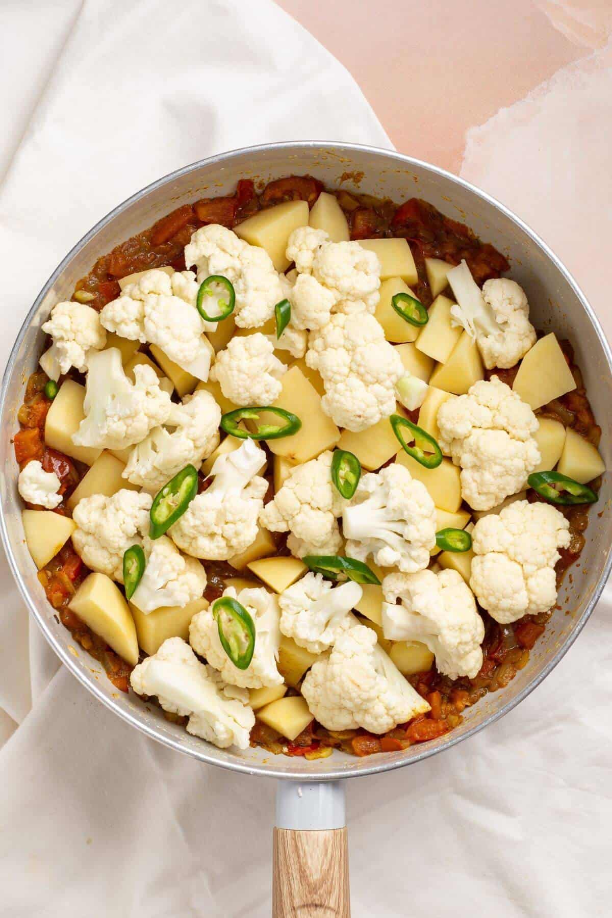 Potatoes, cauliflower, and green chili pepper added to skillet.