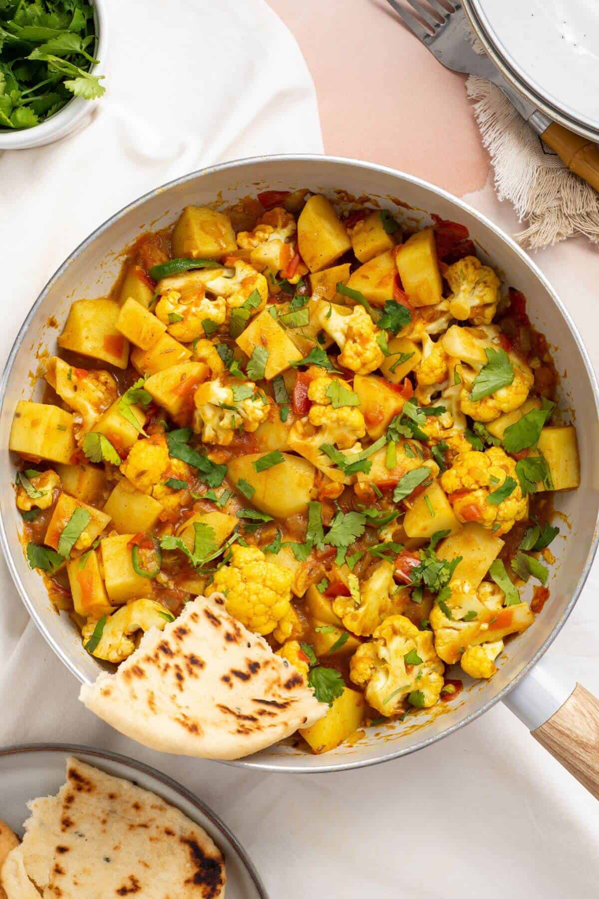 Finished potato and cauliflower dish in skillet with piece of naan bread.