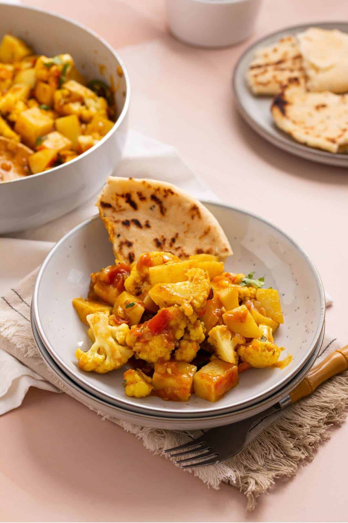 Serving of aloo gabi masala in bowl with naan bread.