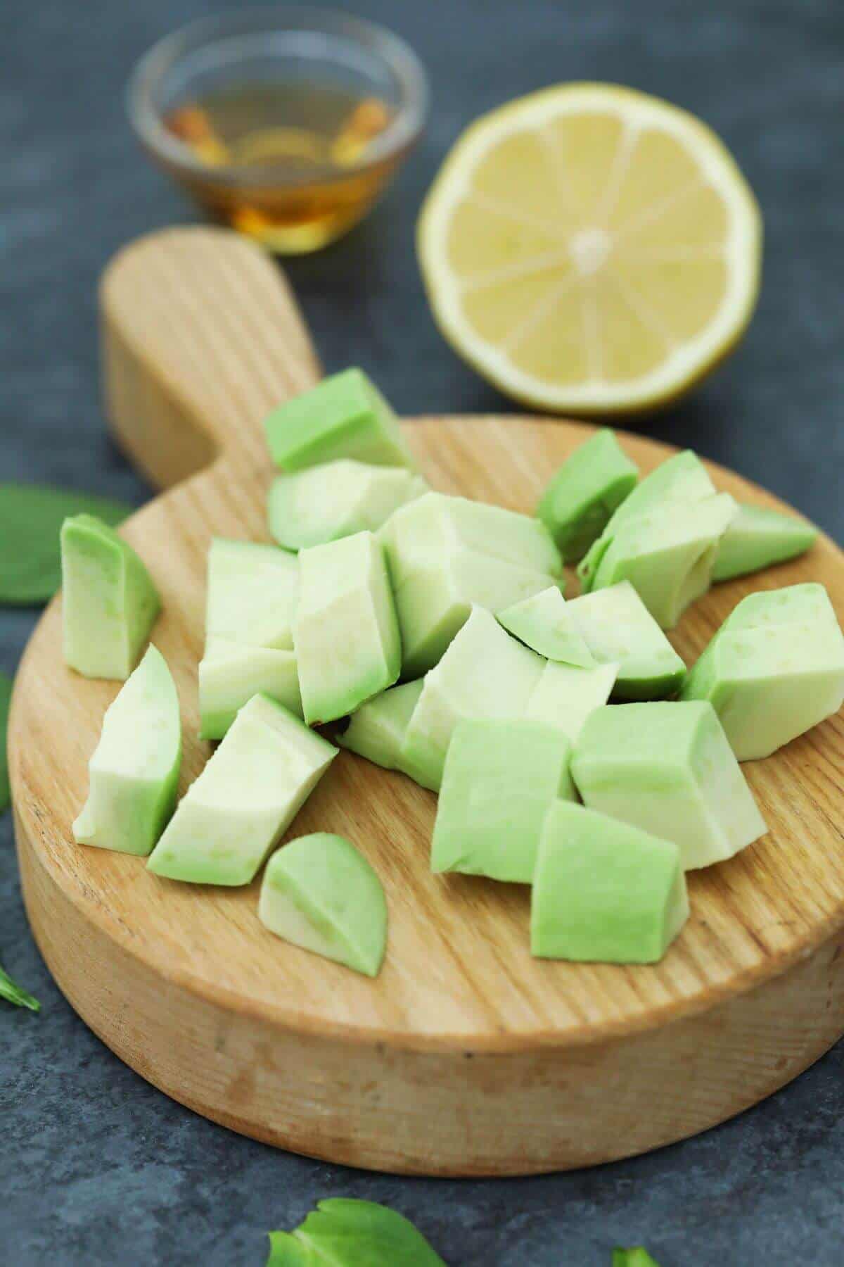 Avocado chunks on a wooden cutting board with lemon and honey in back.