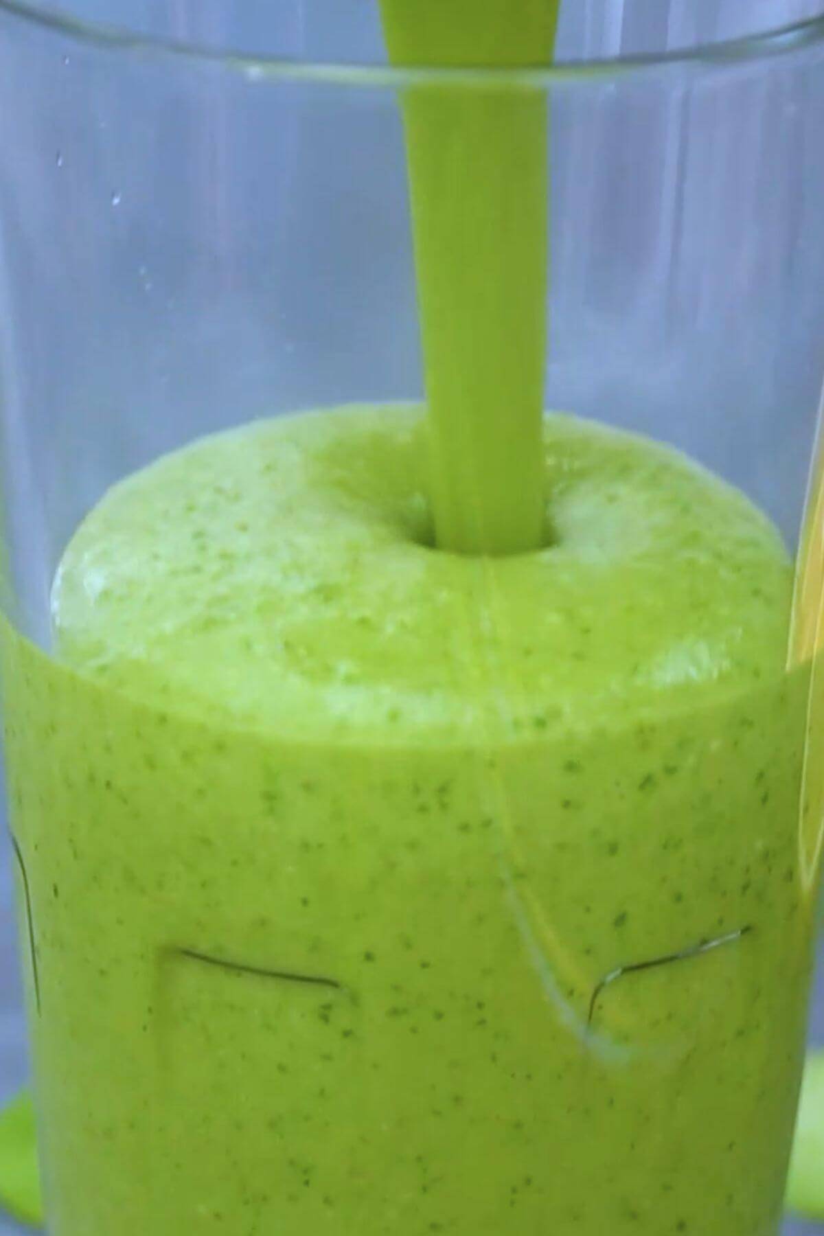 Pouring green smoothie into tall glass.