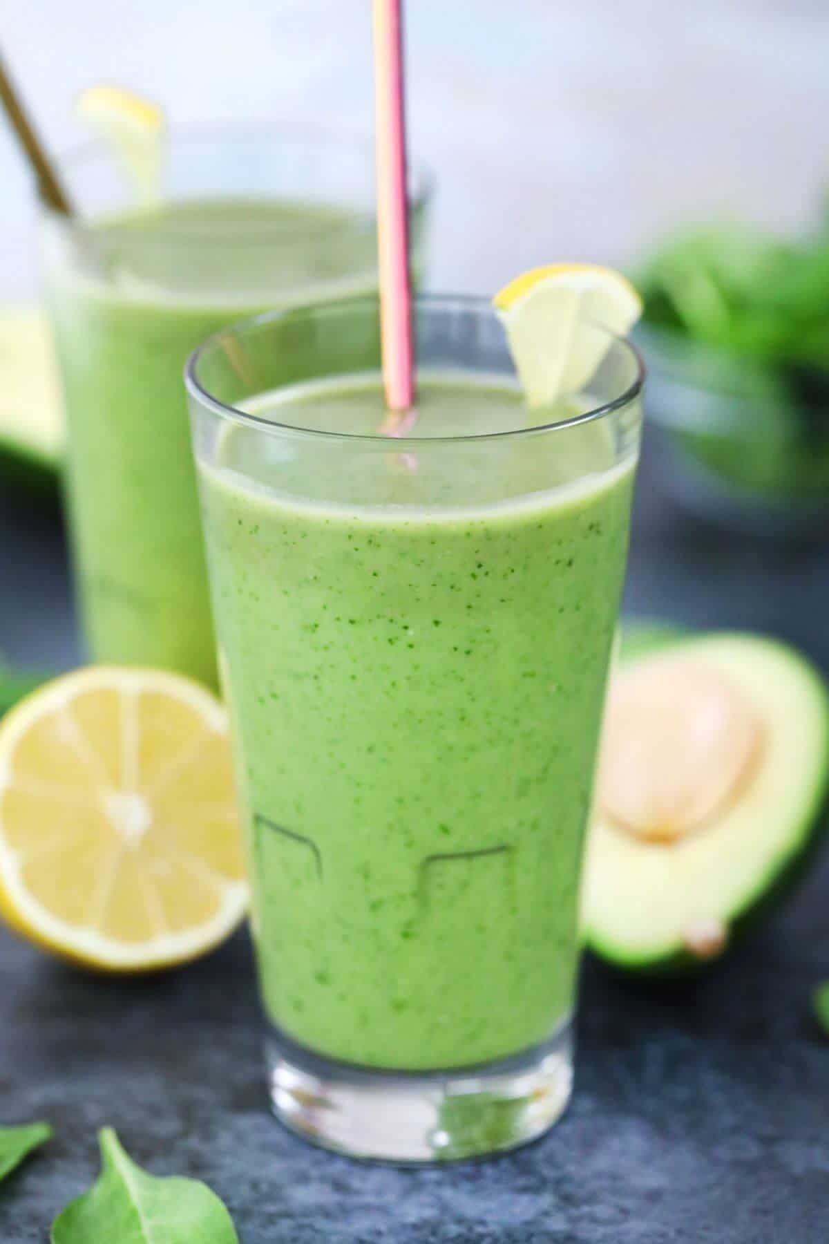 Two tall glasses with green beverages and striped straws garnished with lemon wedges.