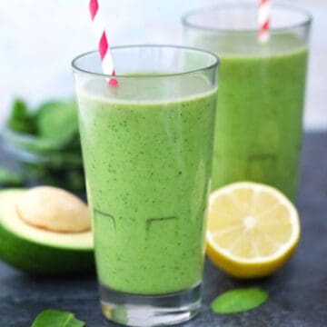 Two tall glasses with avocado spinach smoothie and striped straws.