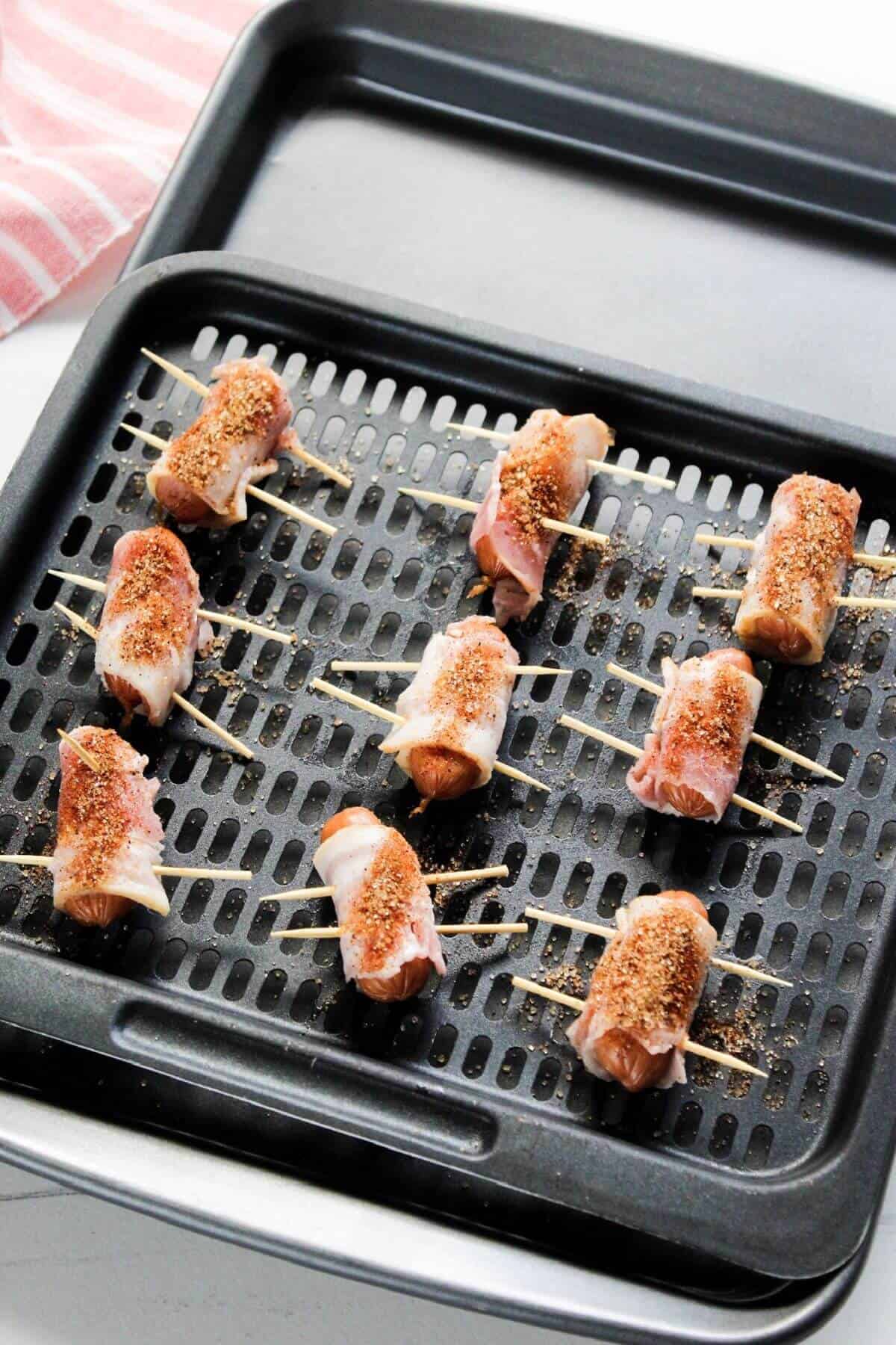 Bacon wrapped smokies on air fryer tray with seasoning sprinkled on.