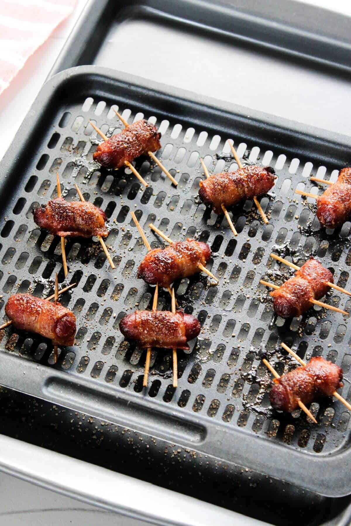 Cooked bacon wrapped little smokies on air fryer tray.