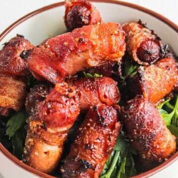 A bowl filled with bacon wrapped little smokies on a bed of leafy greens.