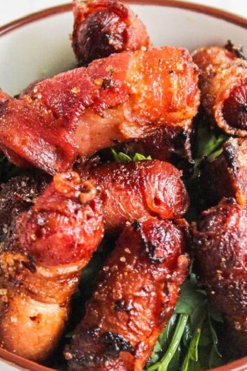A bowl filled with bacon wrapped little smokies on a bed of leafy greens.