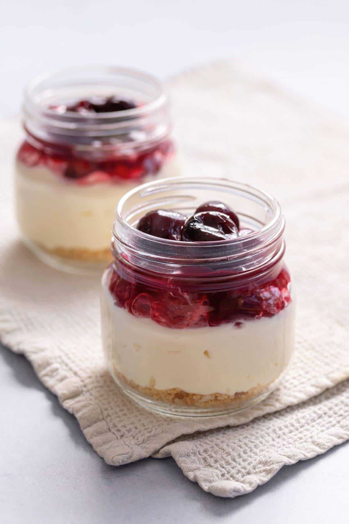 Cherry topping added to top of no-bake cheesecake in jars.