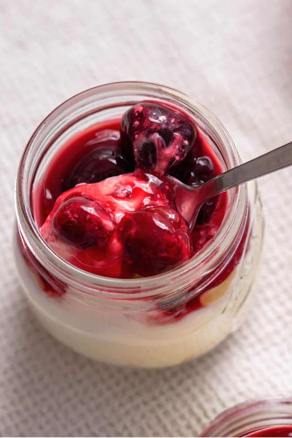 View of spooned cherry cheesecake in jar.
