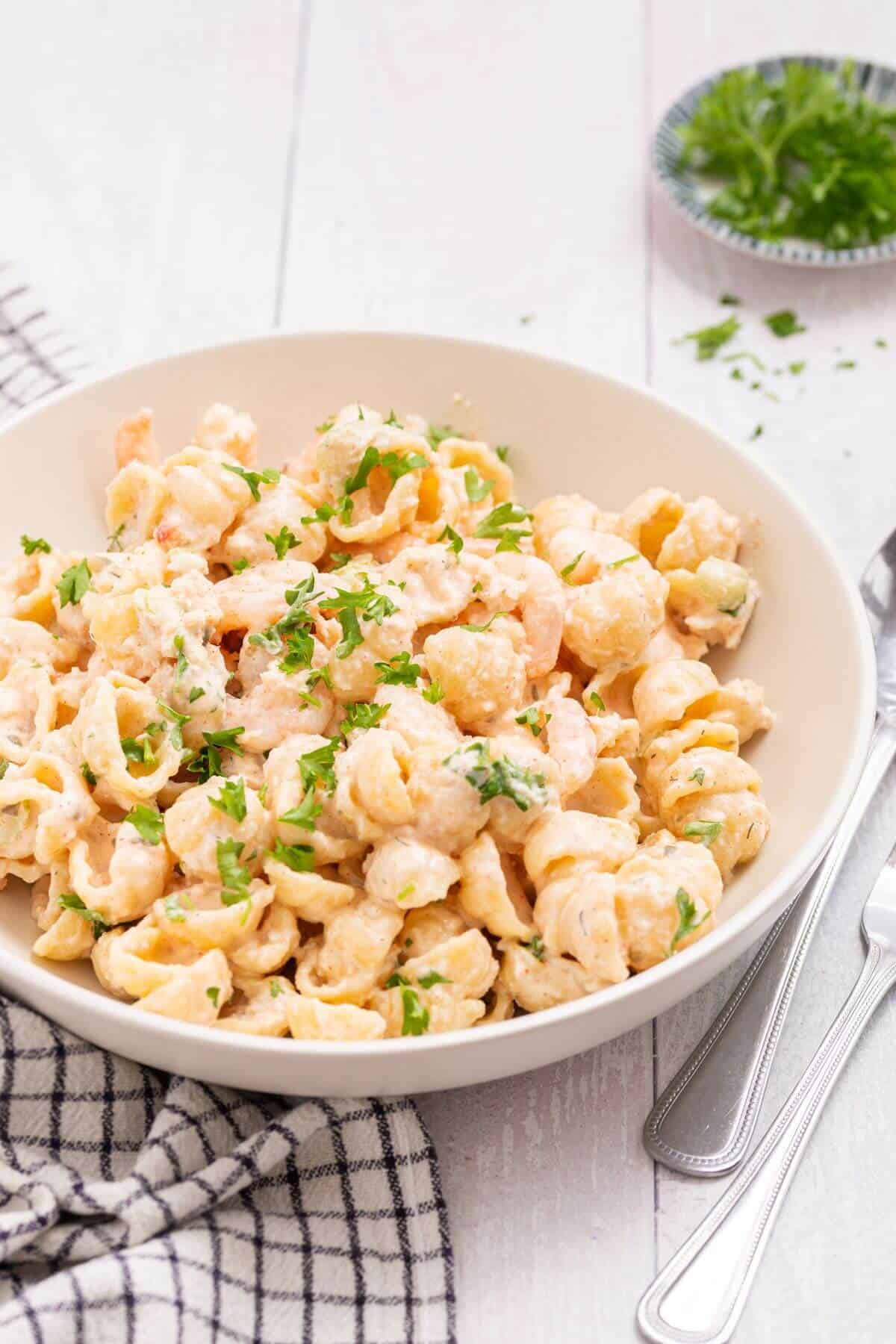 Seafood pasta salad in a white serving bowl with fresh chopped parsley.