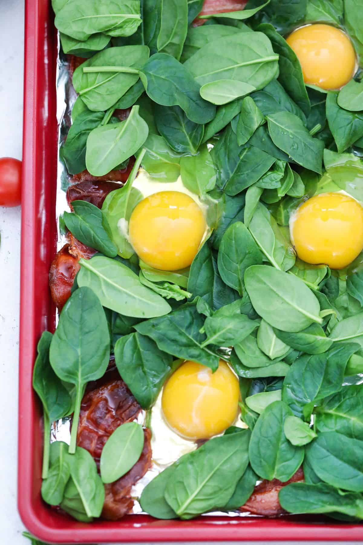Baby spinach and eggs added to bacon in sheet pan.