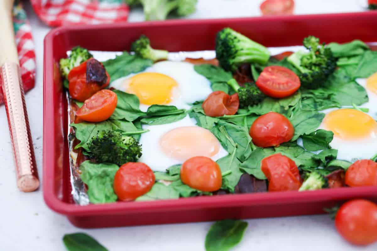 Sheet pan with cooked eggs, spinach, tomatoes, broccoli, and bacon.