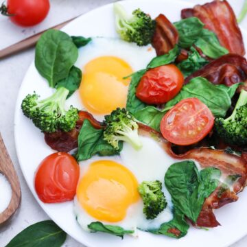 Sheet pan eggs with vegetables and bacon served on a white plate.