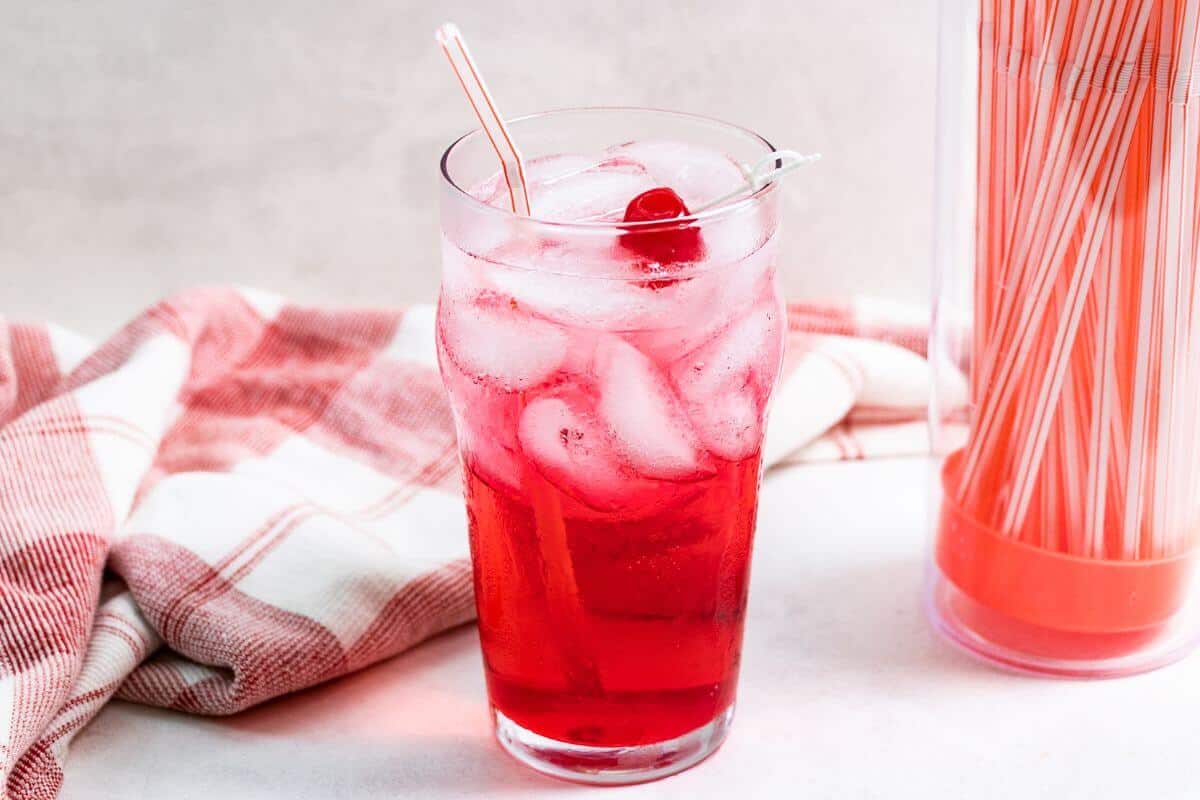 Shirley temple drink in tall glass with container of straws.