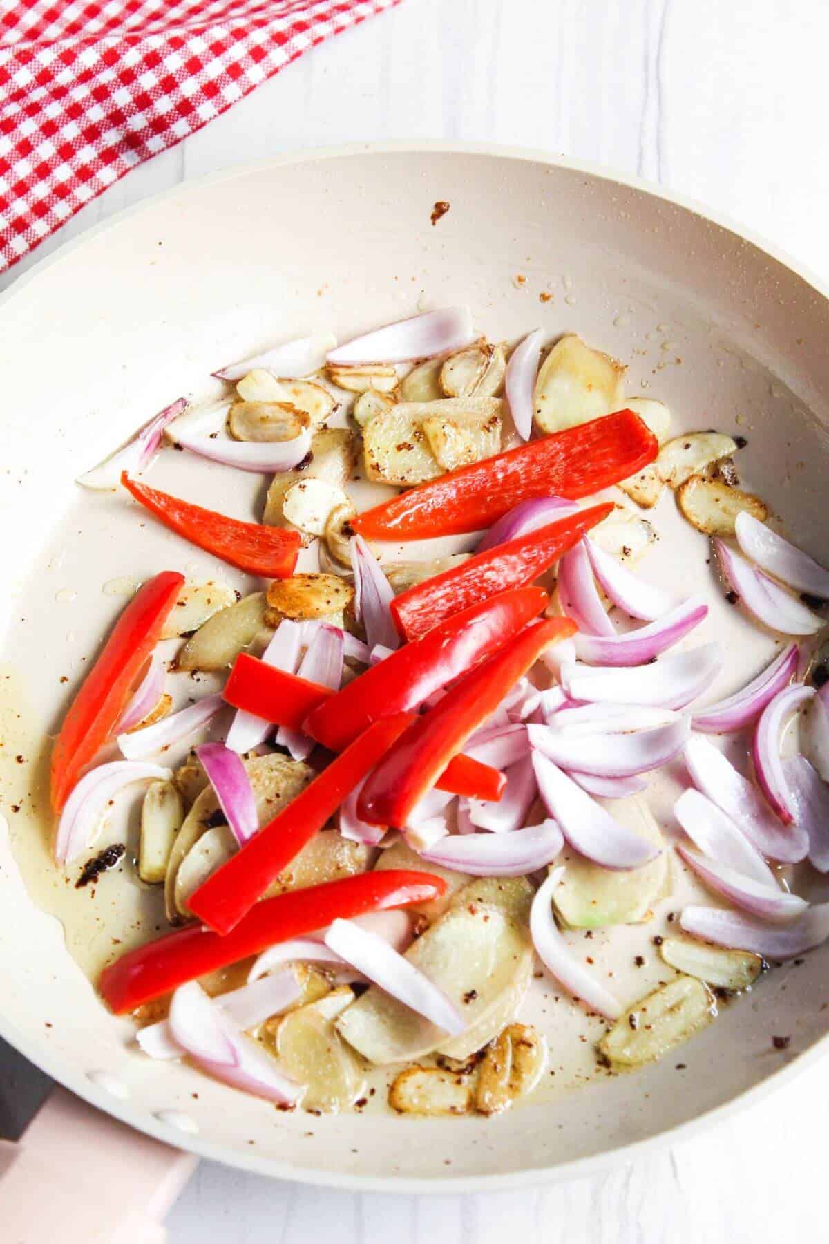 Cooking red bell pepper and onion in skillet.