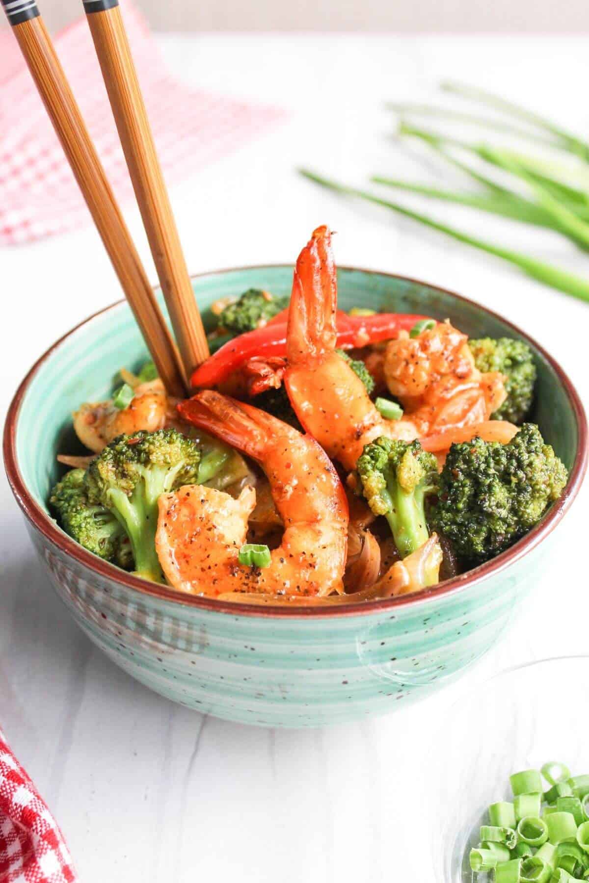 Chopsticks in bowl of shrimp and broccoli stir fry.