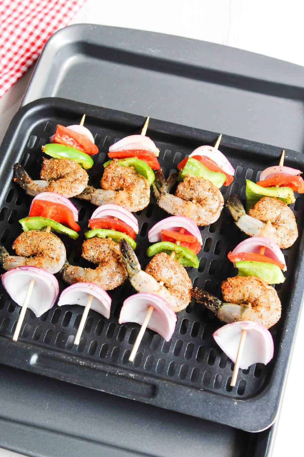 Uncooked shrimp kebobs on air fryer tray.