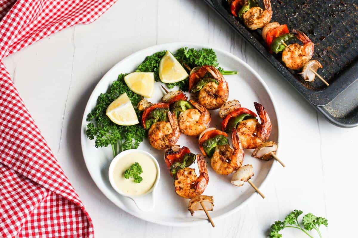 Grilled shrimp skewers on plate with lemons and dip.