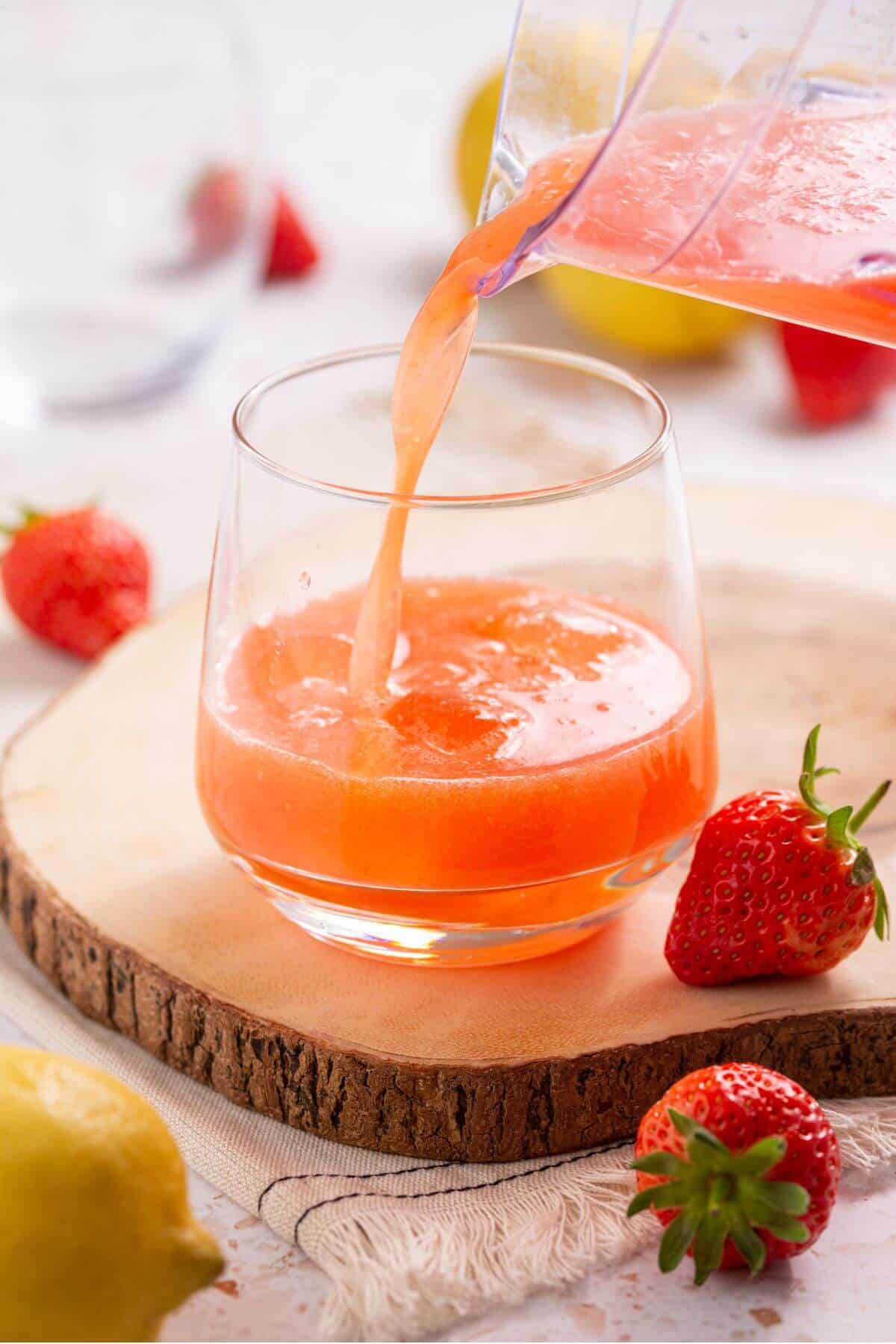 Pouring strawberry lemonade into a glass.