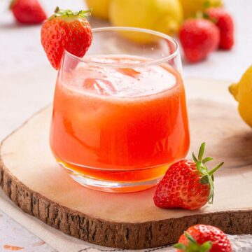 Glass of strawberry lemonade with strawberries and lemons.