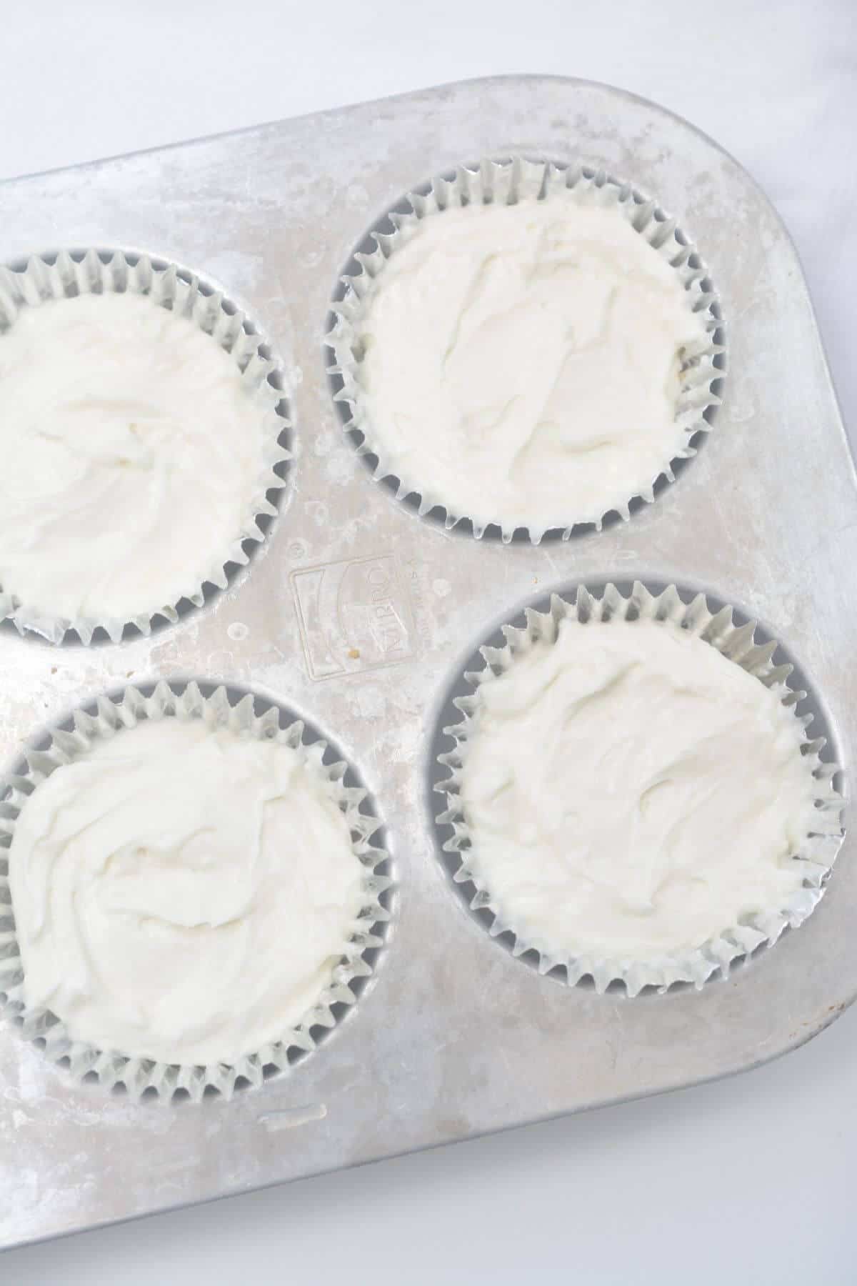 Vegan cheesecake filling spread over crust in muffin pan.