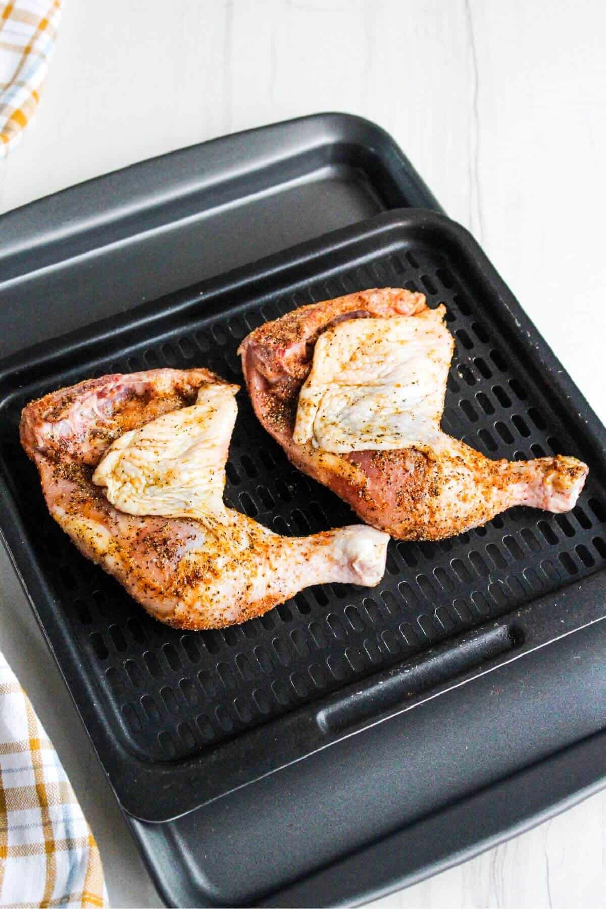Partially cooked chicken legs on air fryer tray.