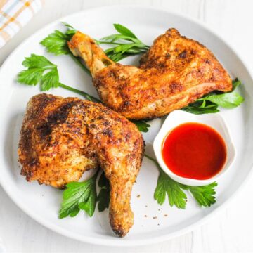 Air fryer chicken legs on plate with parsley and dipping sauce.