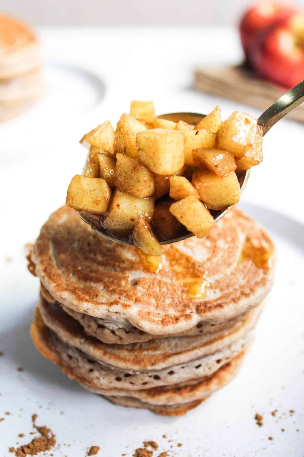 Adding apple topping to a stack of pancakes.