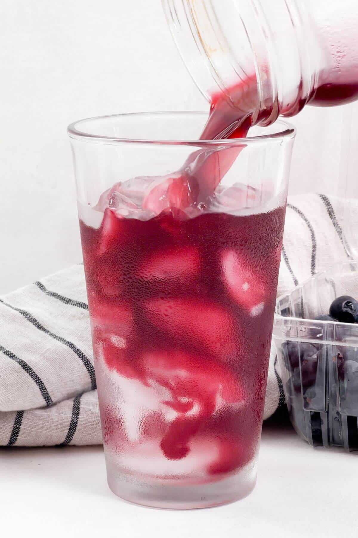 Pouring blueberry lemonade mixture into glass with ice.