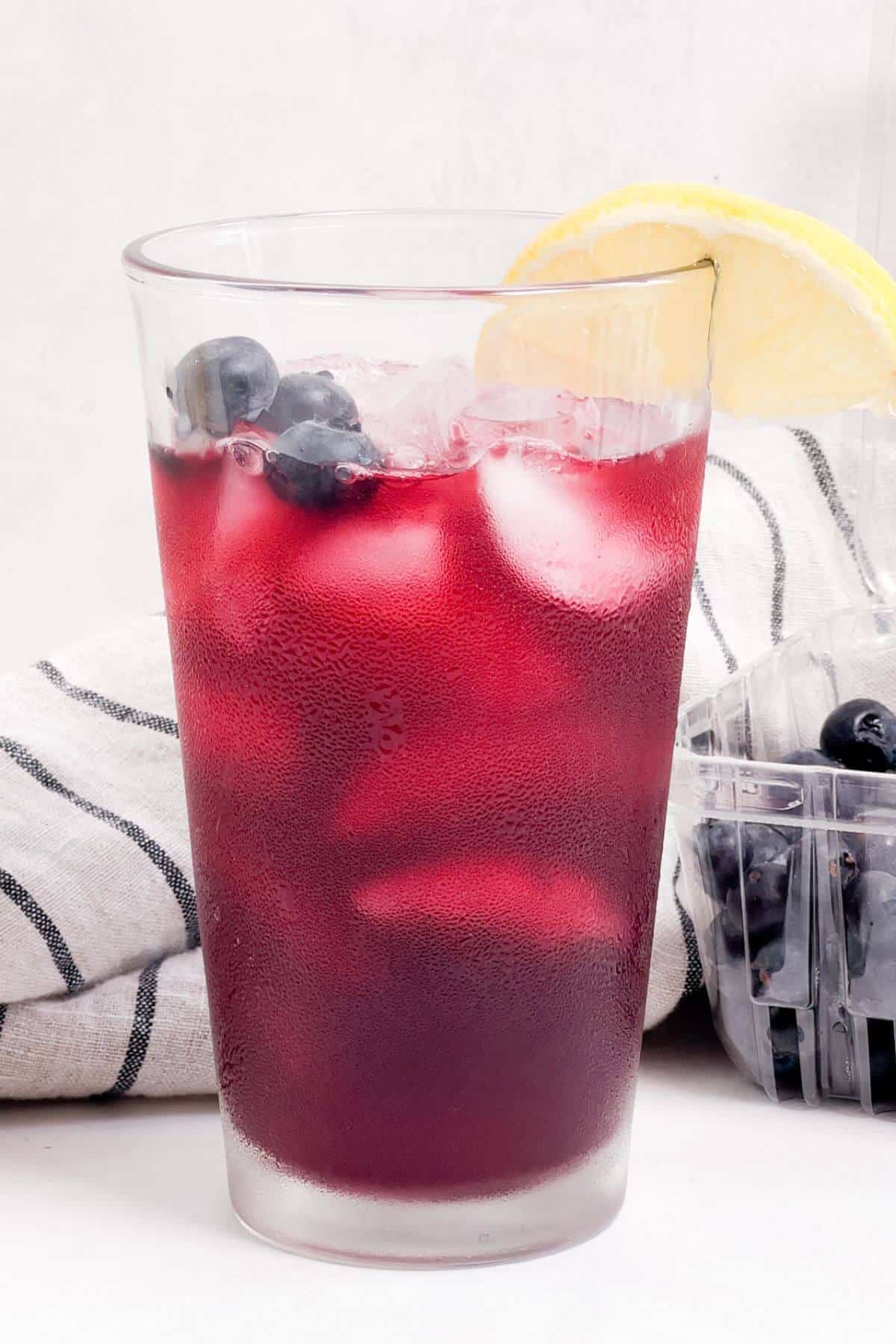 Garnishing blueberry lemonade cocktail with fresh lemon slice.