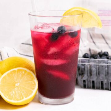 Blueberry vodka lemonade with sliced lemon and container of blueberries.