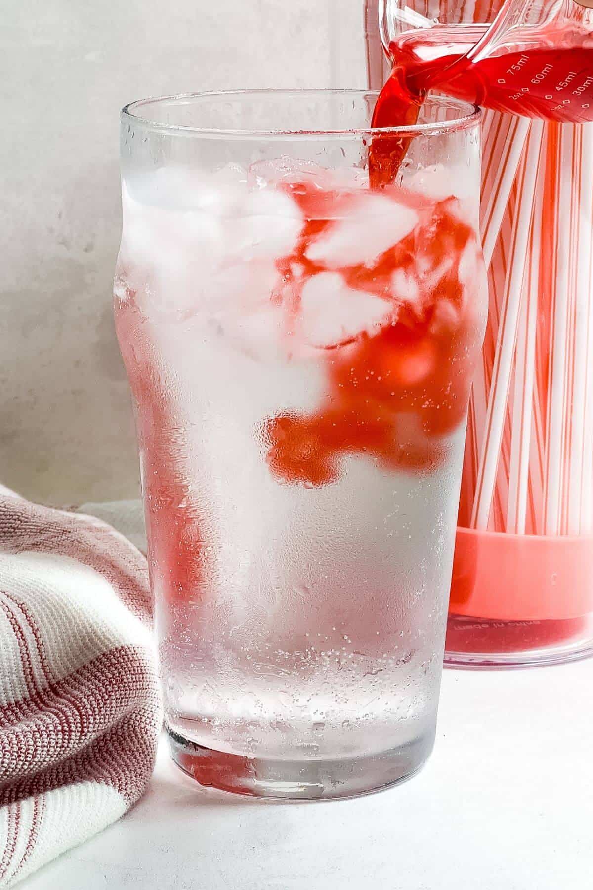 Adding cherry juice to glass of sprite and ice.