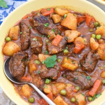 A bowl of easy beef stew with chunks of beef, potatoes, carrots, peas, and a spoon, garnished with parsley.