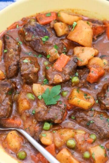 A bowl of easy beef stew with chunks of beef, potatoes, carrots, peas, and a spoon, garnished with parsley.