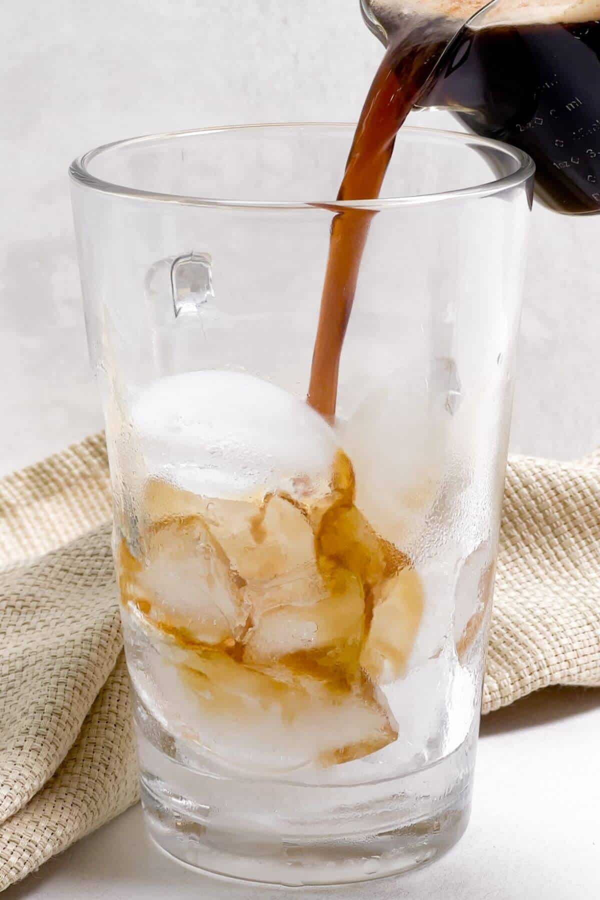 Pouring brewed espresso over ice in tall glass.