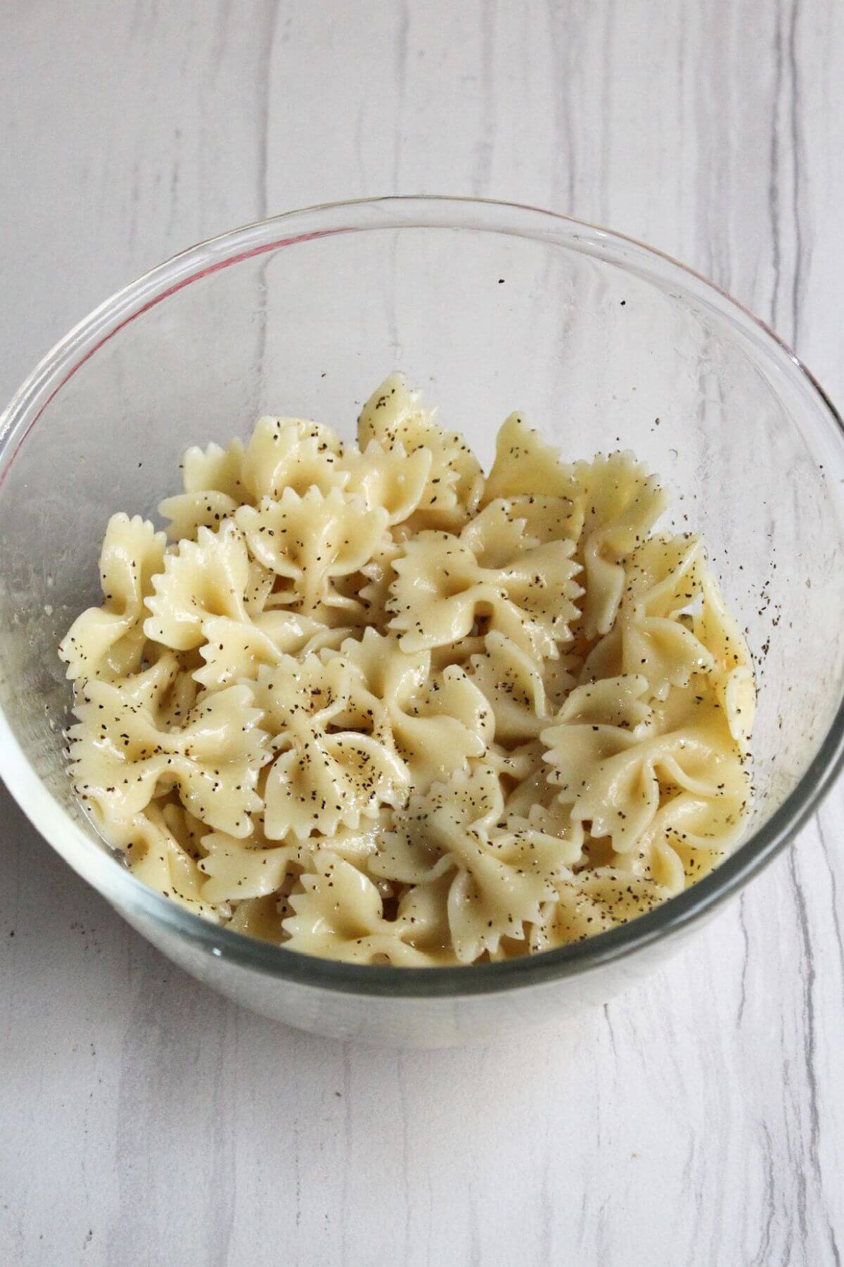 Cooked bowtie pasta in bowl with ground black pepper.
