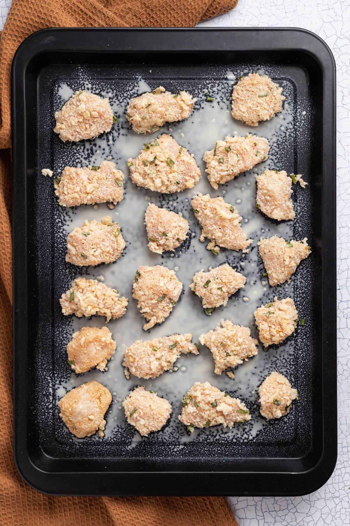 Coated chicken pieces on a baking sheet.