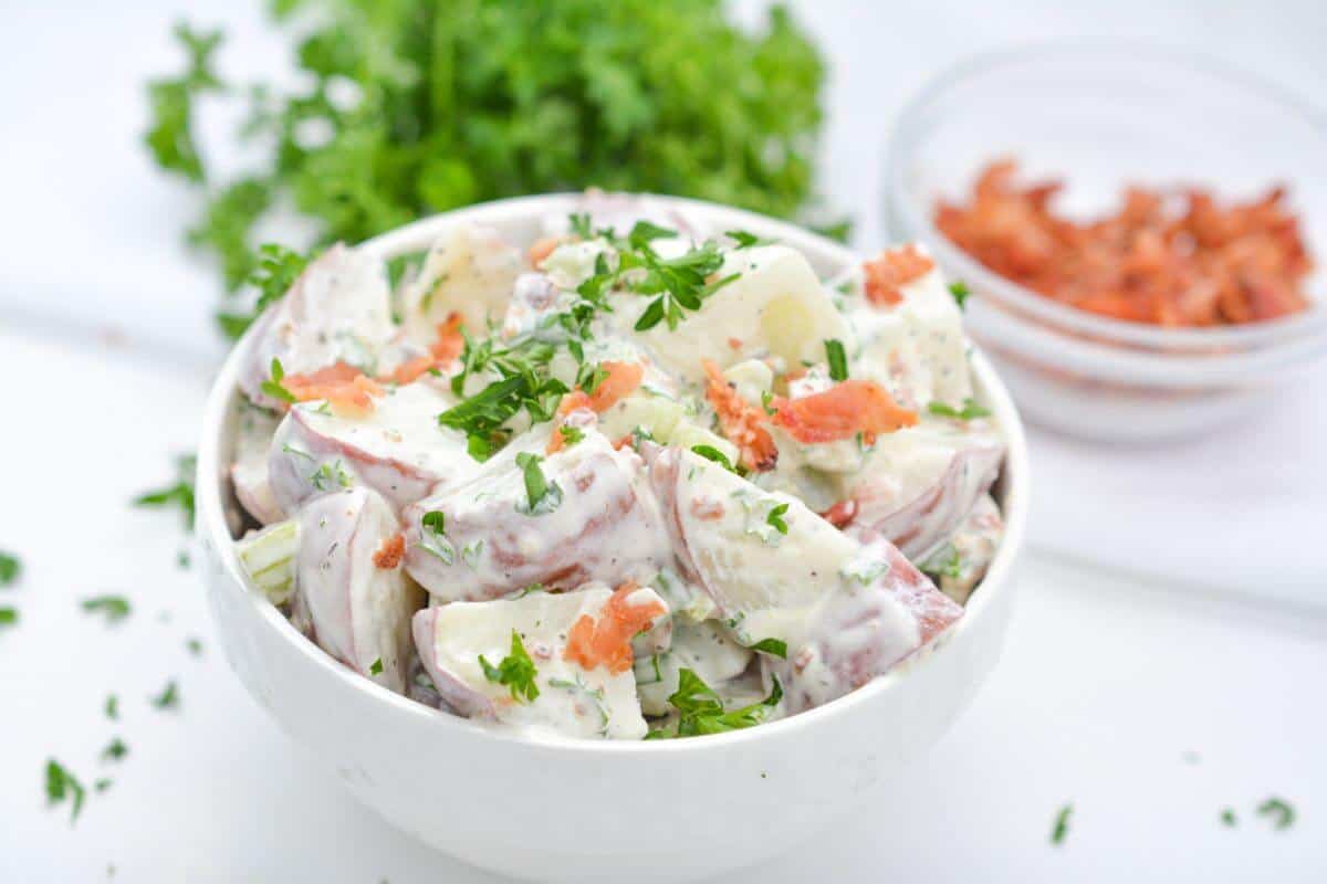 Red potato salad in bowl with bacon and parsley garnish.