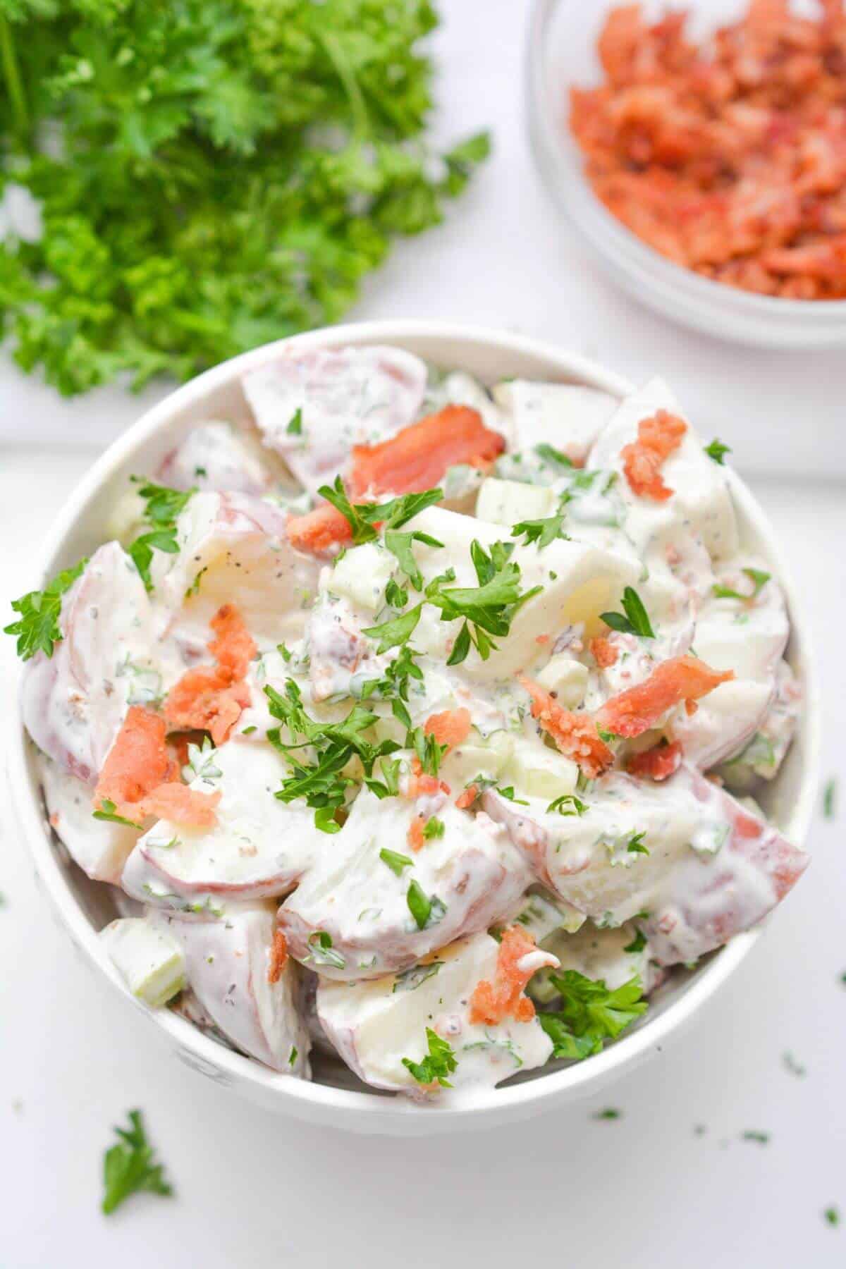 Overhead view of potato salad in bowl with parsley and chopped bacon.