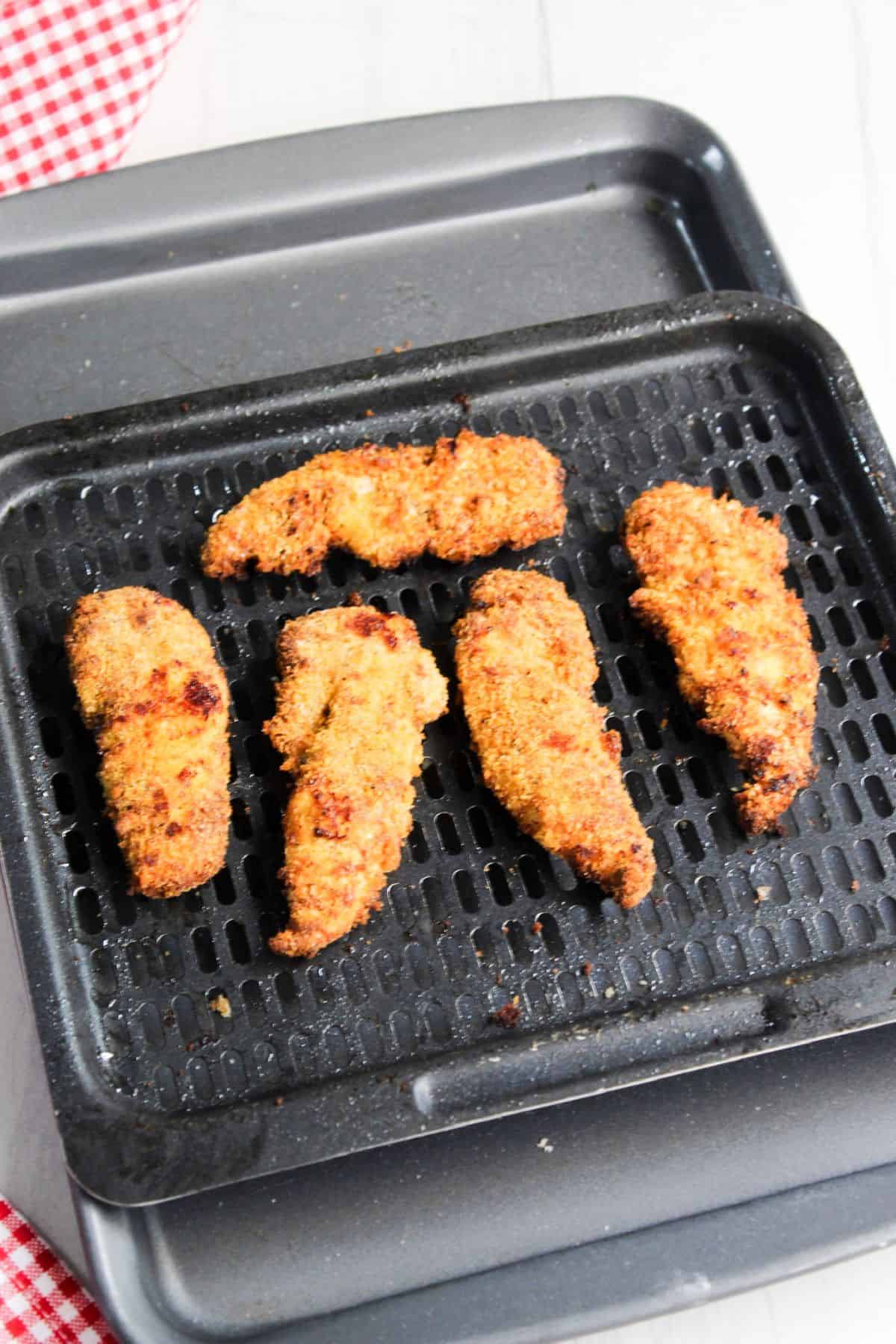 Air fryer chicken tenders on tray with a checkered tablecloth.