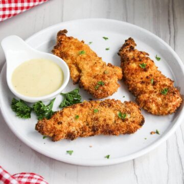 Fried chicken tenders on a white plate with dipping sauce.