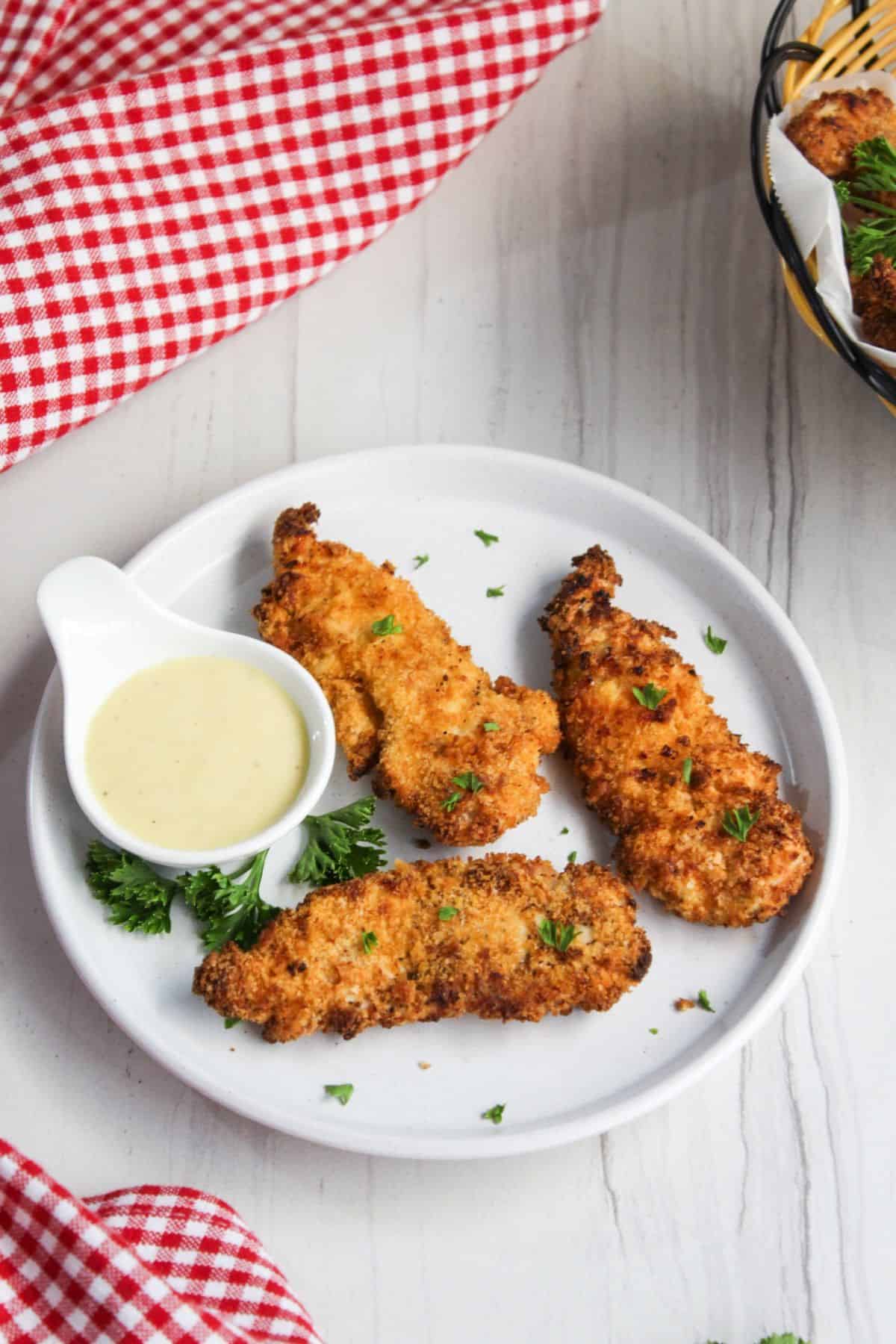 Chicken tenders with dipping sauce on a white plate.