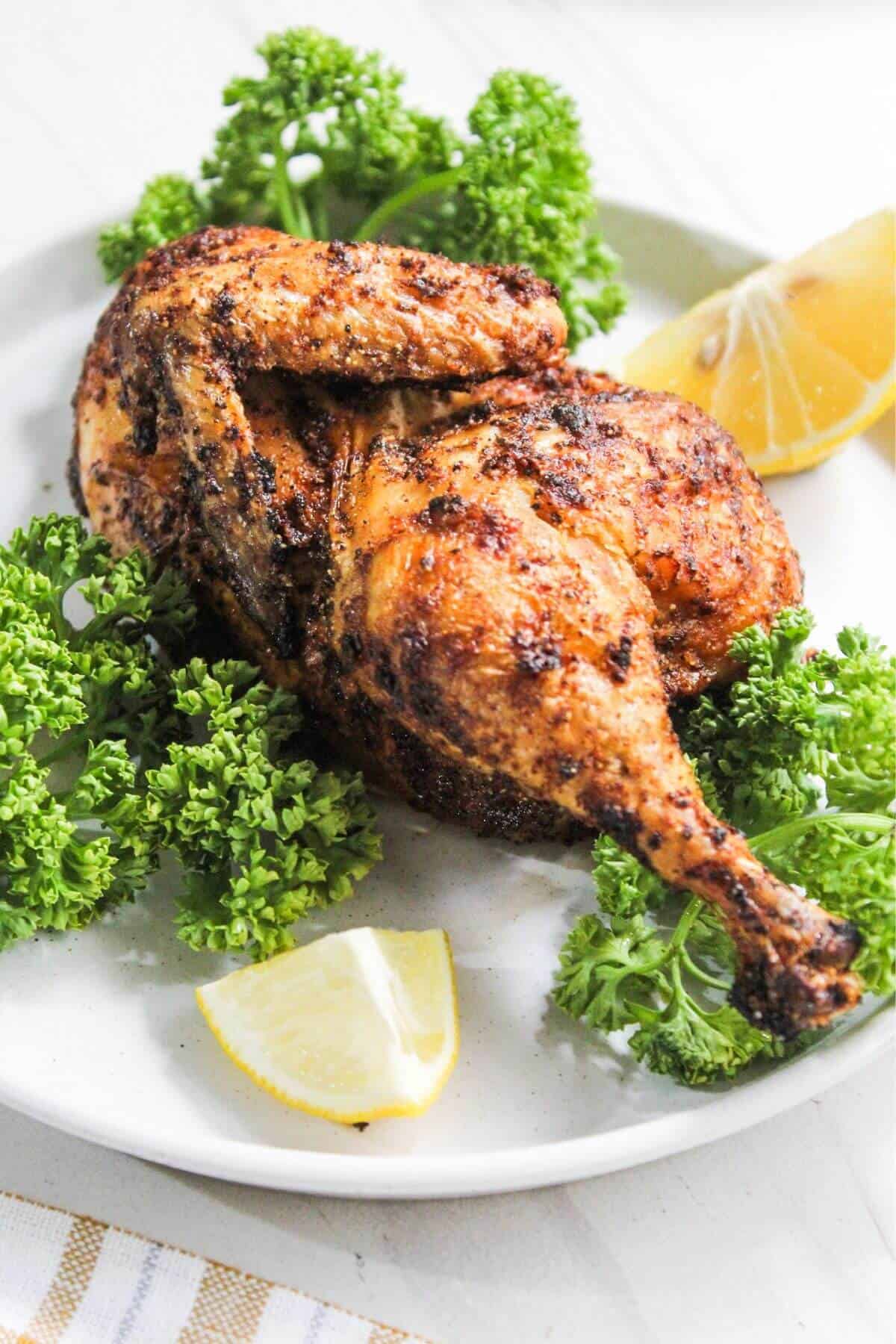 Serving of cornish hen on plate with parsley and lemon wedges.