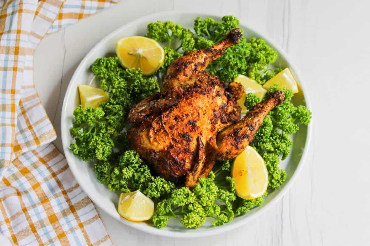 Air fried cornish hen on plate with lemons and parsley.