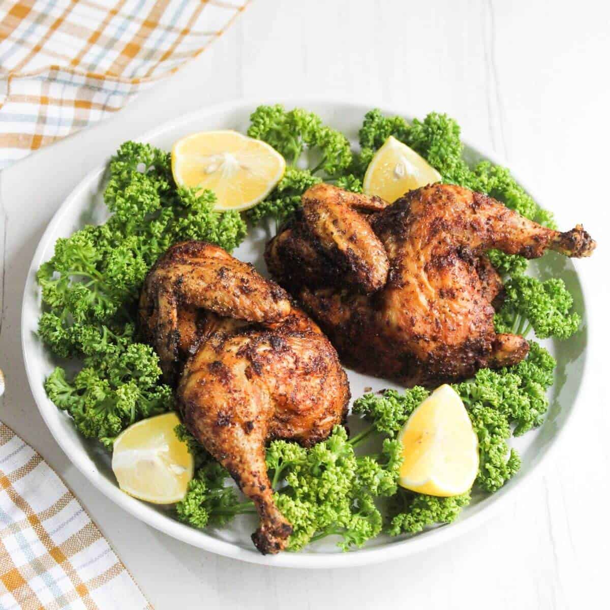 Cornish hen halves on plate with parsley and lemon wedges.