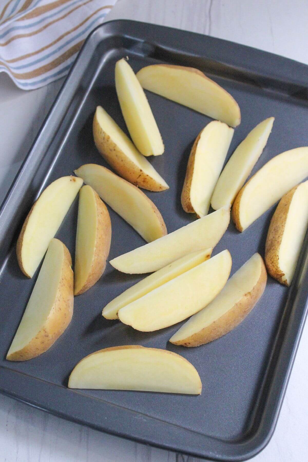 Prepared potato wedges on baking sheet.