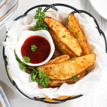 Air fryer potato wedges with dip in paper lined basket.