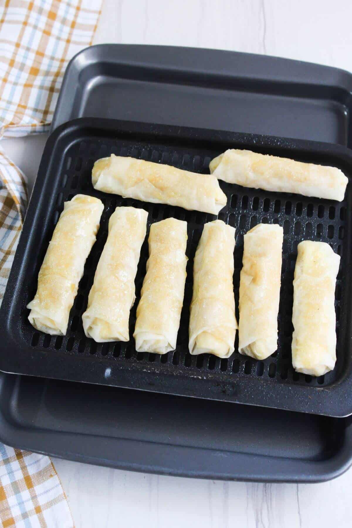 Air fryer tray with rolls of banana turon on it.