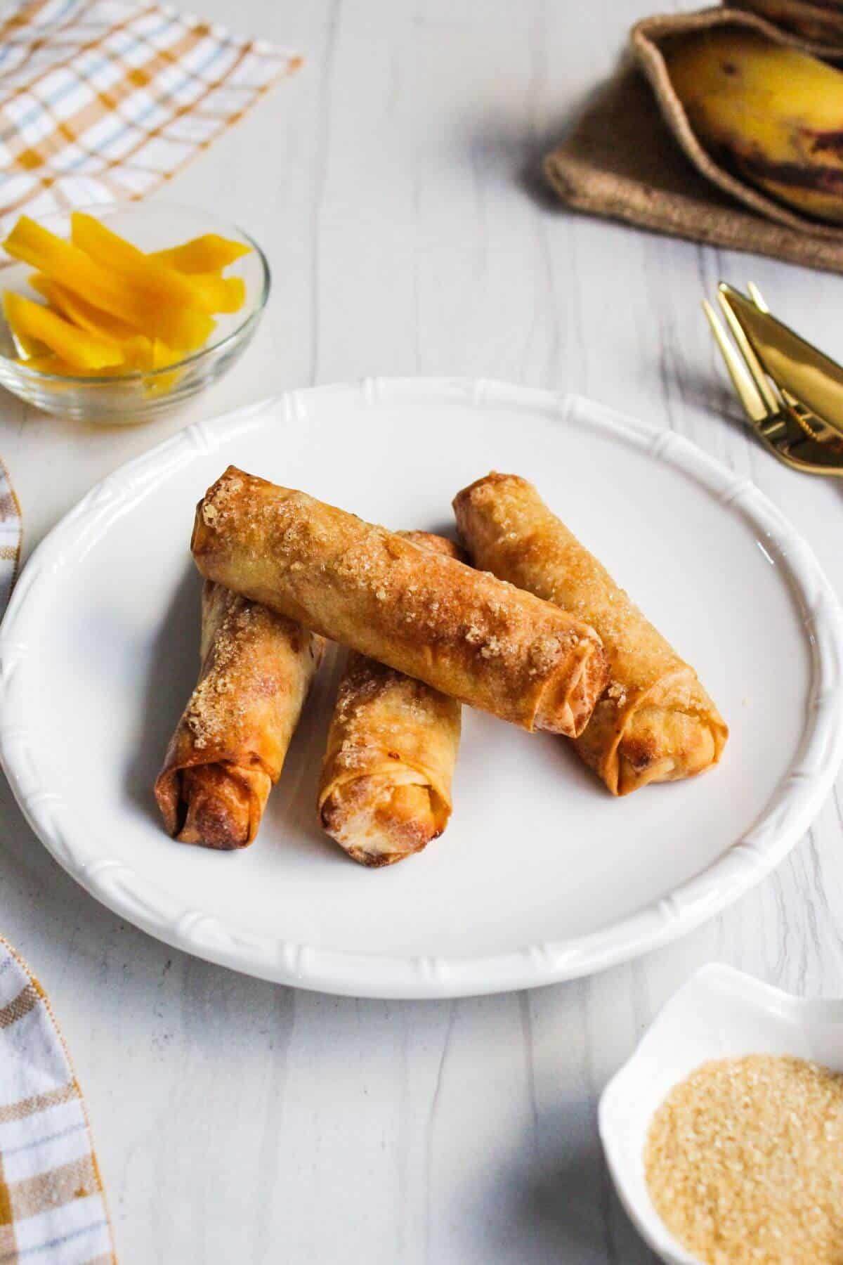 Banana turon spring roll rolls on a white plate with a fork.